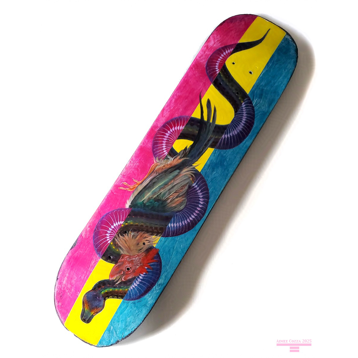 A photograph of a skateboard deck laid on a white table. The skateboard is pink, yellow, and blue in the background. Painted on the deck is a slithering black rainbow boa, coiled up around an American rooster that has been strangled to death. Parts of the snake intersecting the pink and blue areas "xray" view to show the snake's skeleton.
