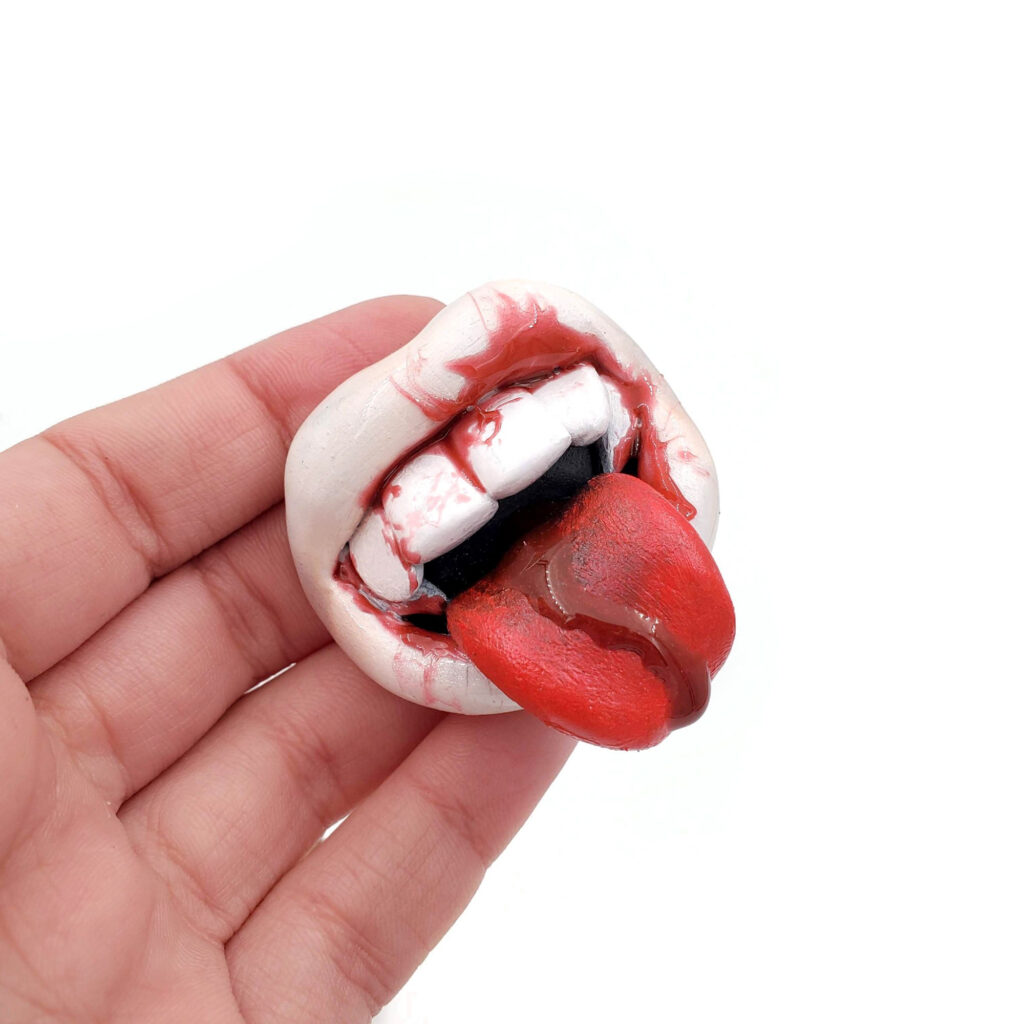 A polymer mouth with white lips, blood dripping out of the mouth and tongue. It's held in a human hand.